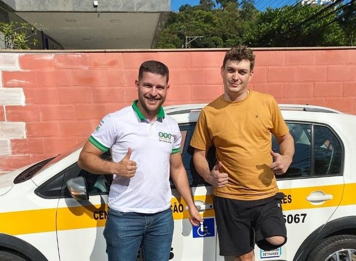 Instrutor e aluno comemorando ao lado do veículo de exame da autoescola