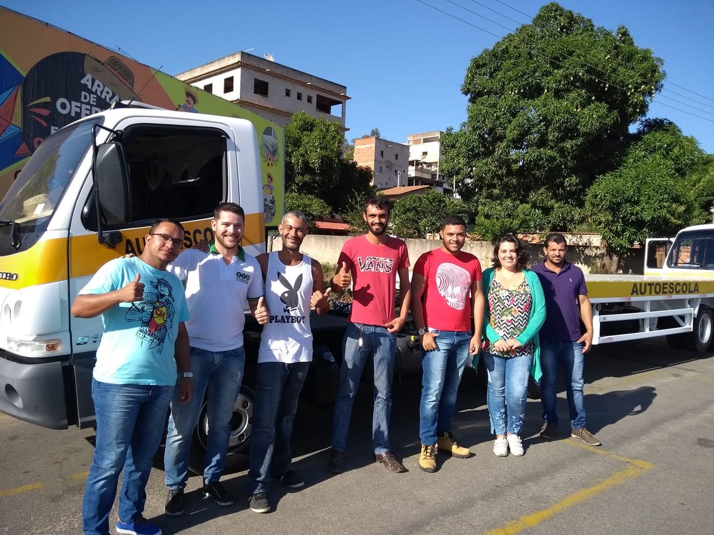 Grupo de alunos aprovados posando ao lado do caminhão prancha da autoescola